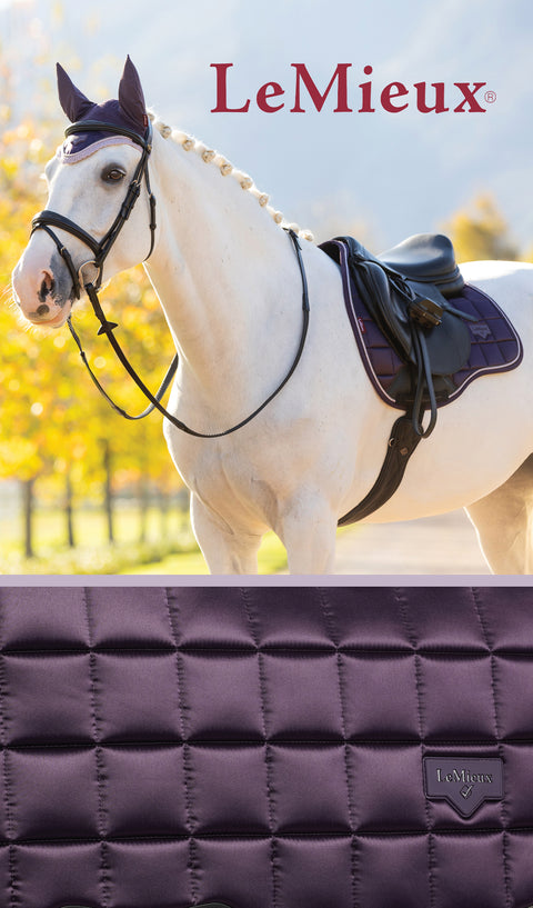 White horse wearing a dark purple ear bonnet and saddle pad with black saddle. LeMieux logo above. Close up of dark purple quilted saddle pad at the bottom.