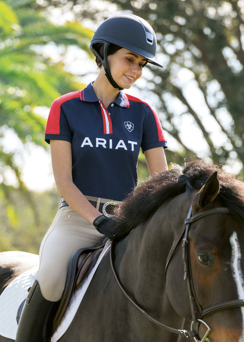 Rider on a dark brown horse wearing a helmet and a blue and red shirt that says Ariat