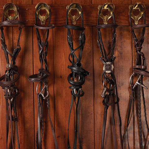 Darkened image of various English bridles hanging in a wooden tack room.