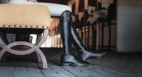 Ariat black tall riding boots being worn on a stone floor with a blurred background