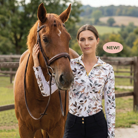 Horse standing with woman, who is wearing a white quarter zip shirt with a pattern of leaves and horses in muted shades of rose and gray.