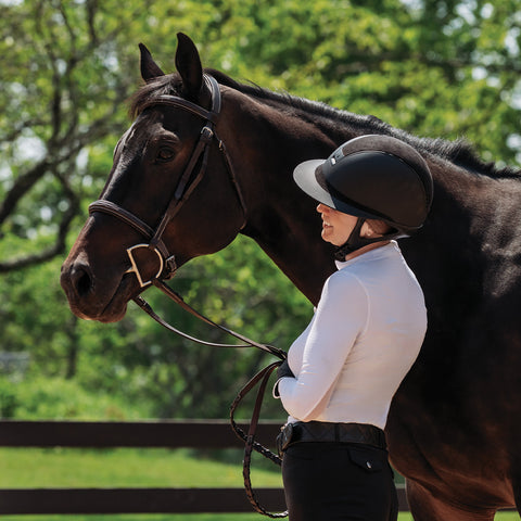 Woman, dressed to ride, smiling at dark bay horse with bridle on.