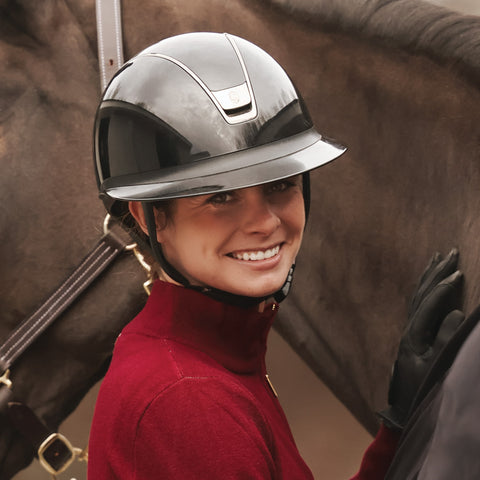 Woman wearing a glossy riding helmet and red shirt next to a horse